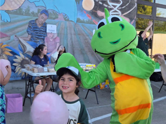 picture of a girl holding a cottton candy with a dragon mascot at the carnival